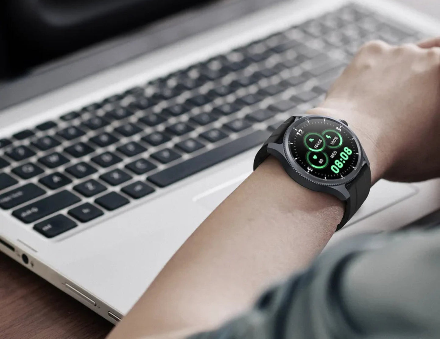 Person wearing a smartwatch with a laptop in the background