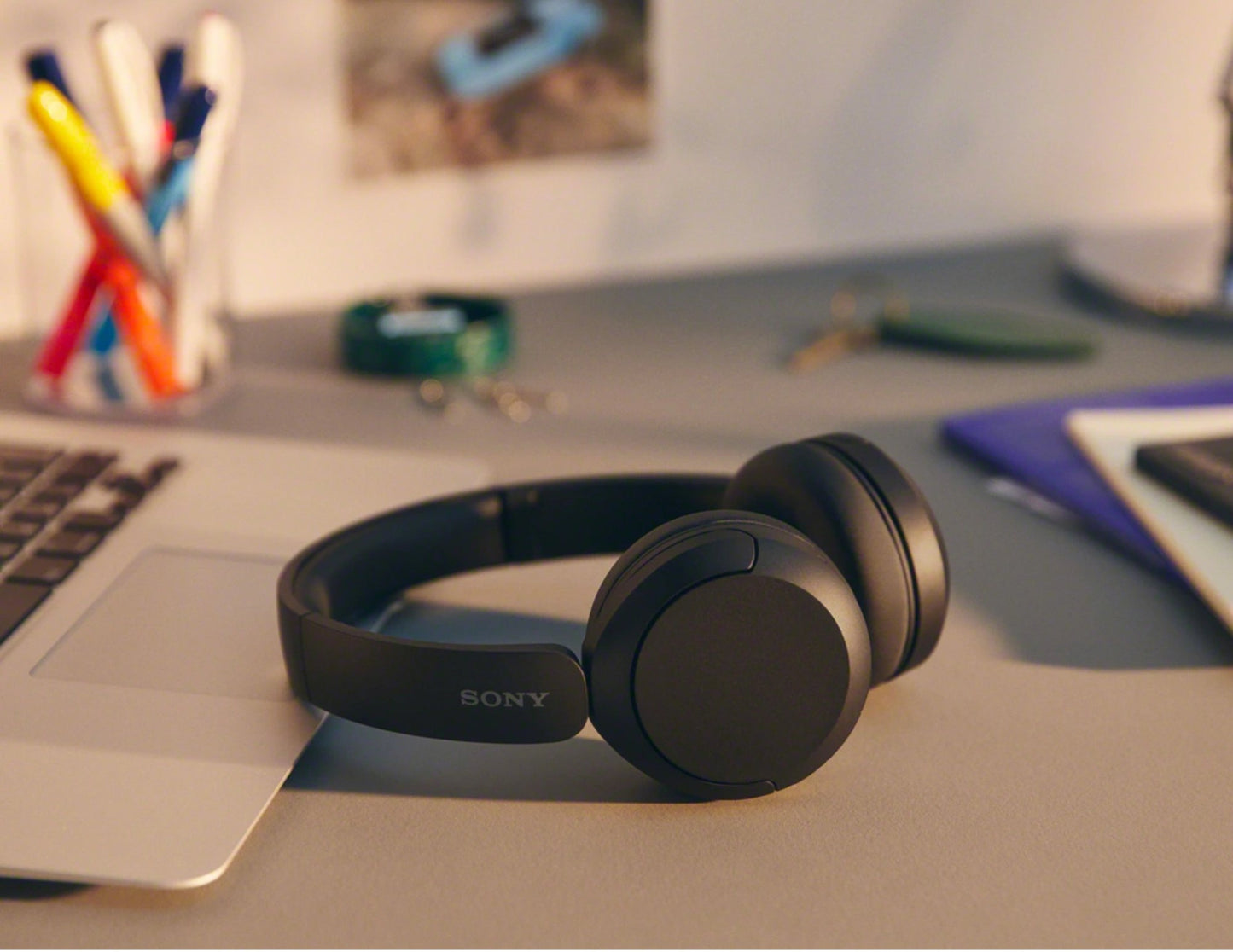 Sony headphones on a desk with a laptop and stationery items in the background