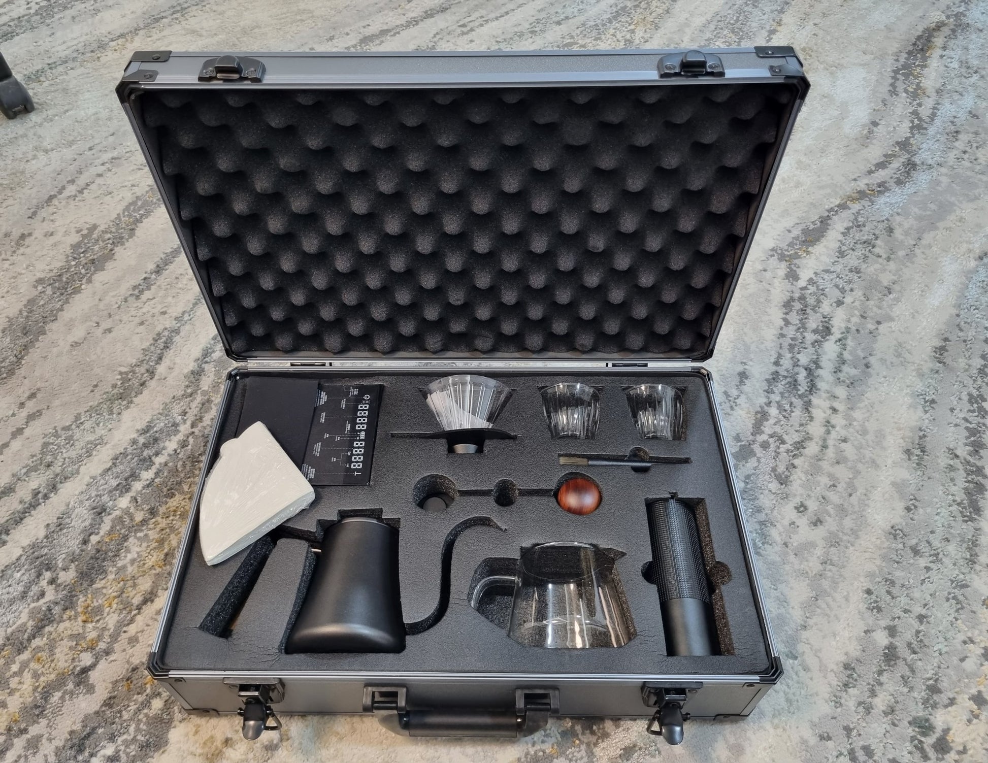 Coffee brewing kit in a black foam-lined case on a textured surface
