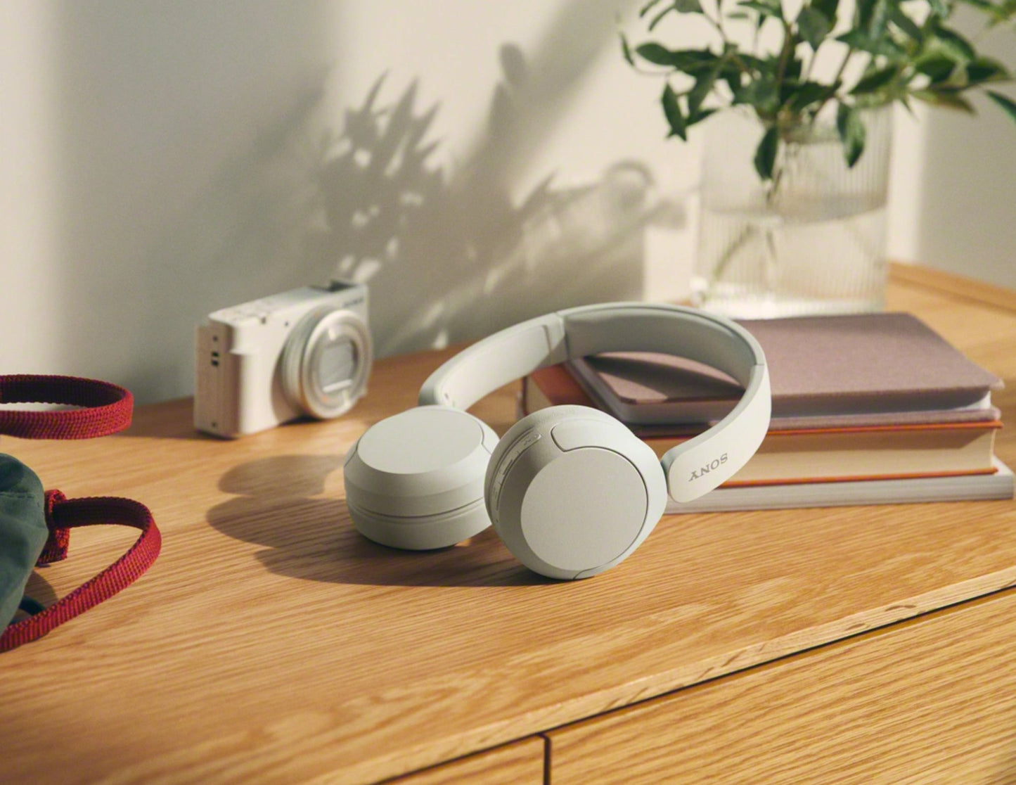 White headphones on a wooden surface with a camera, books, and plant in the background