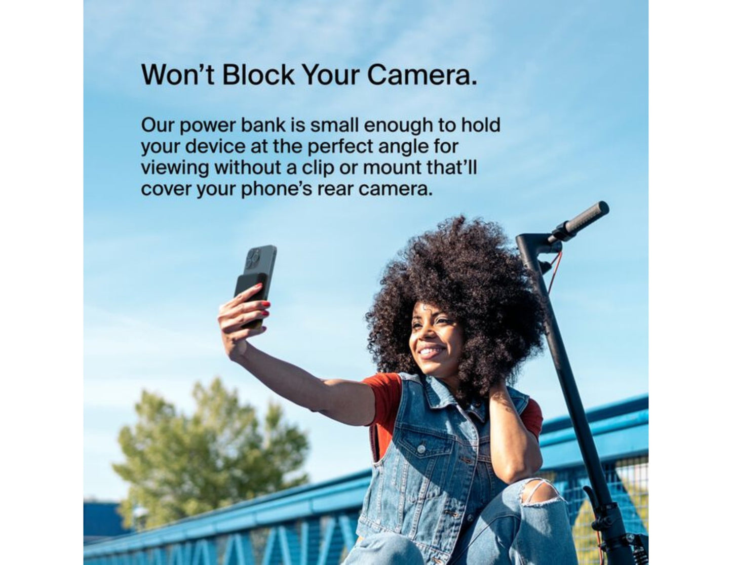 Person using a Belkin BoostCharge Magnetic Wireless Power Bank 5000mAh with Fold-out Stand – BPD004btBK – Black to hold a phone at an angle outdoors with promotional text.