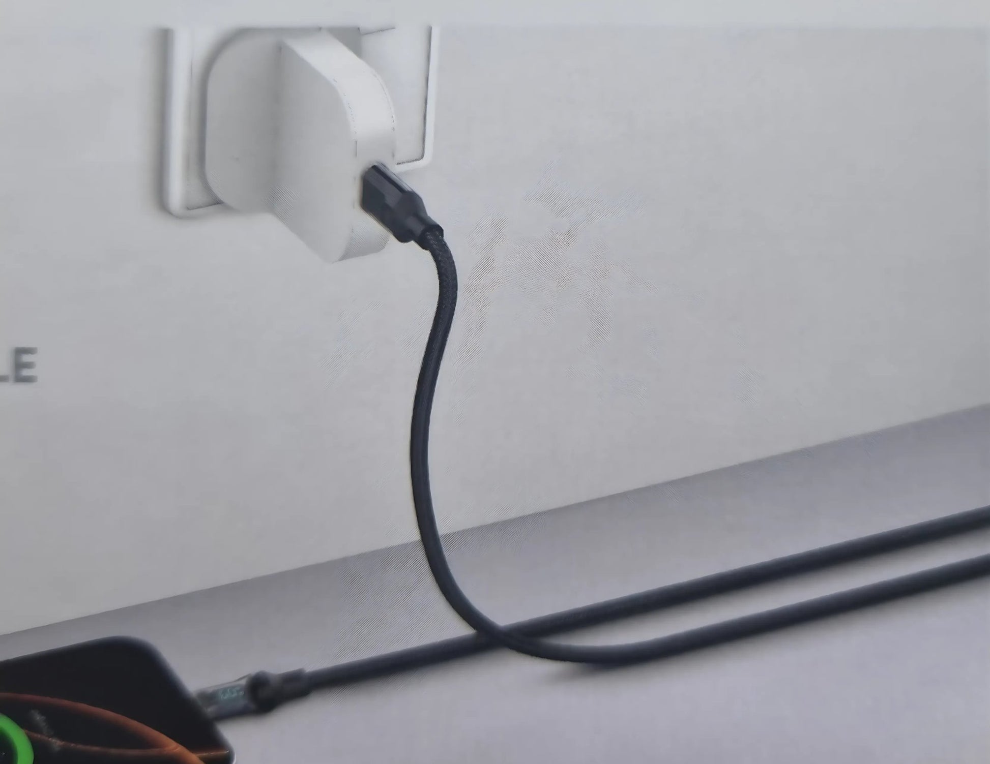 Black cable plugged into a white wall socket on a light gray surface.