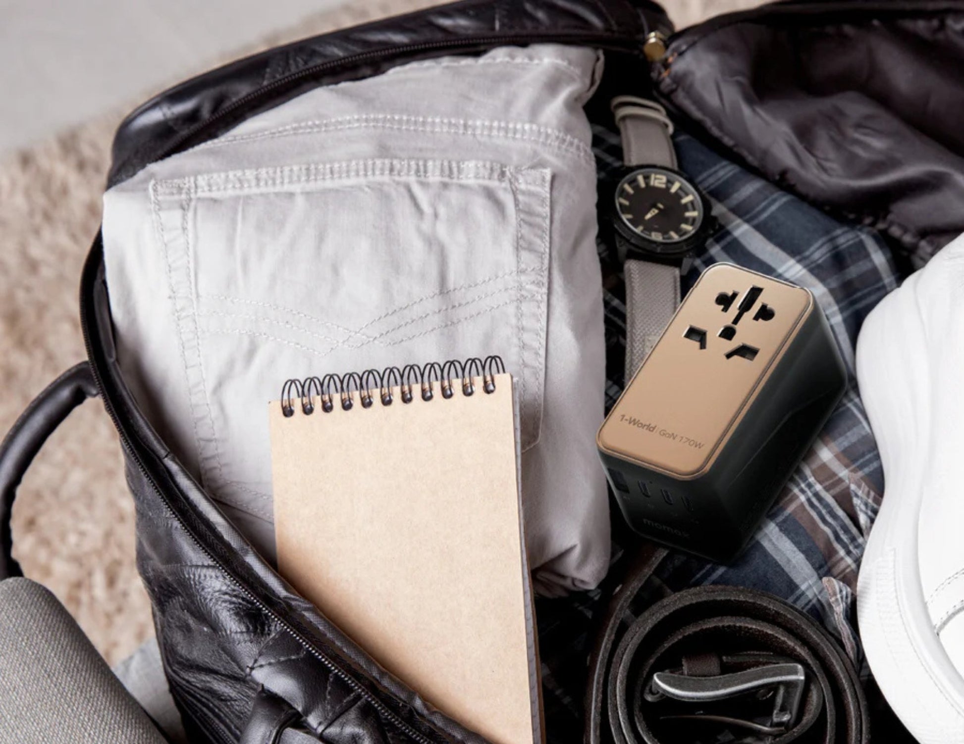 Travel bag with a notebook, watch, and power adapter.