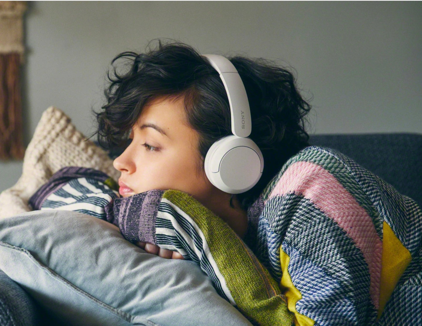 Person wearing headphones and wrapped in a colorful blanket on a couch