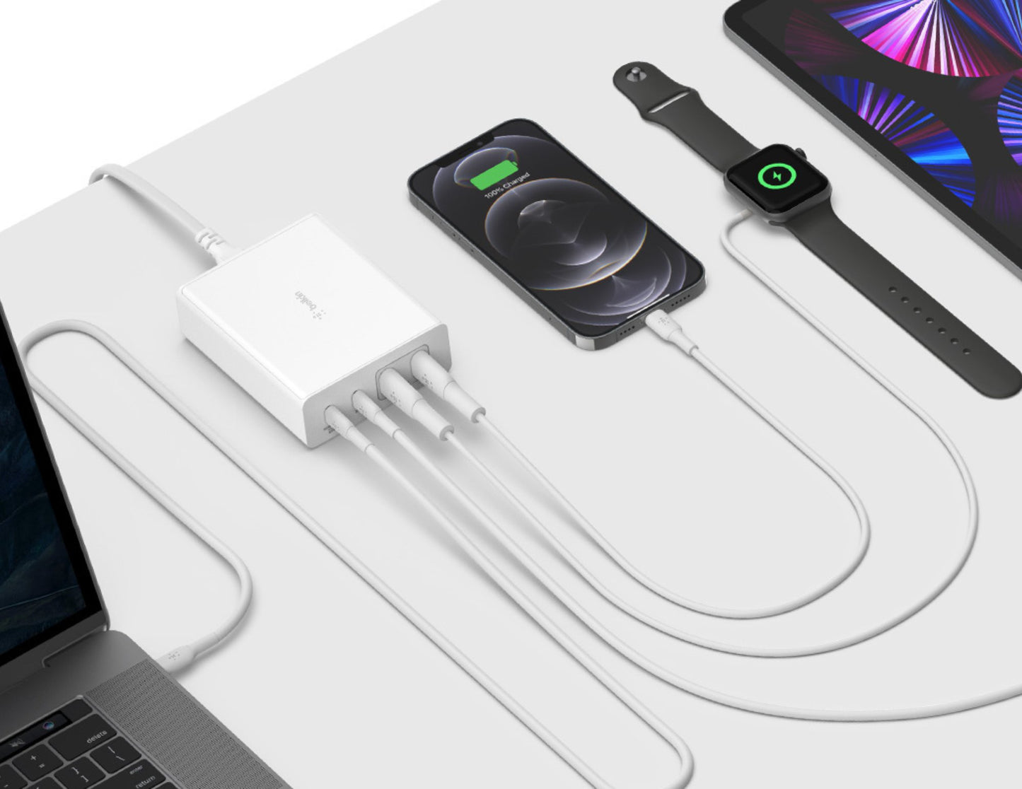 Multiple electronic devices charging on a white surface with a laptop.