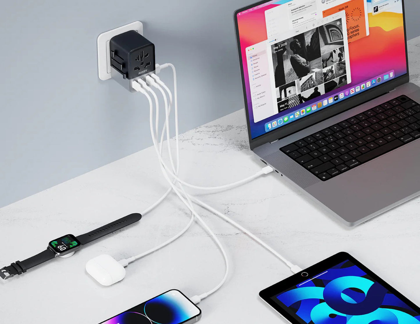 Laptop, smartwatch, smartphone, and tablet charging from a single power adapter on a desk.