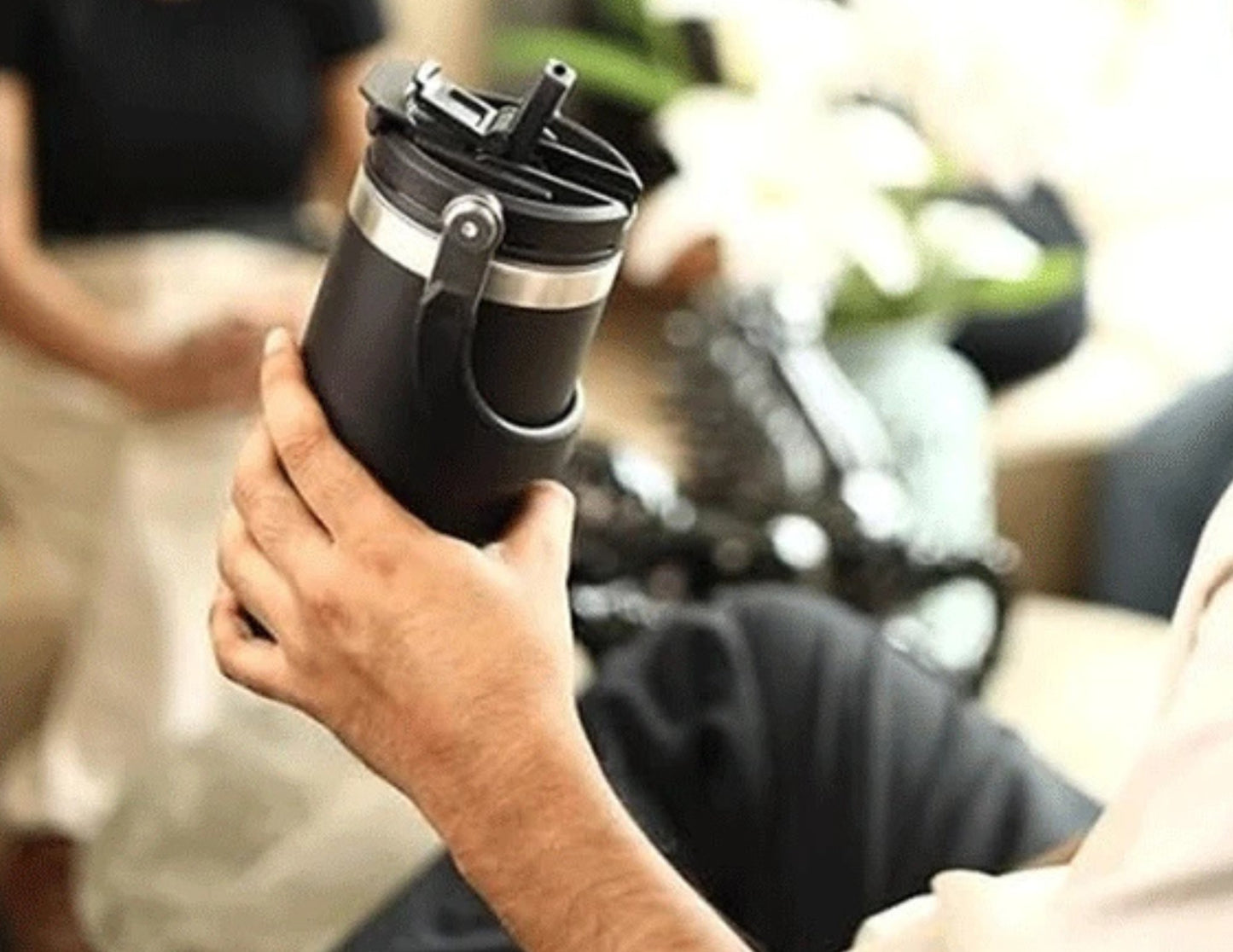 Person holding a black Tyeso TS-8828 Vacuum Insulated Tumbler 900ML – With Handle & Straw Lid with a blurred background