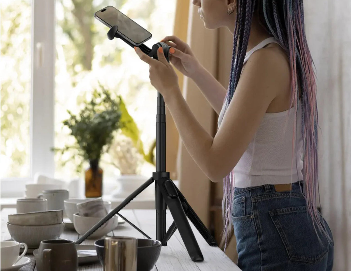 Person using a smartphone with a Momax 1-Snap Pole Magnetic Tripod Selfie Stick with Wireless Remote – KM17D in a kitchen setting