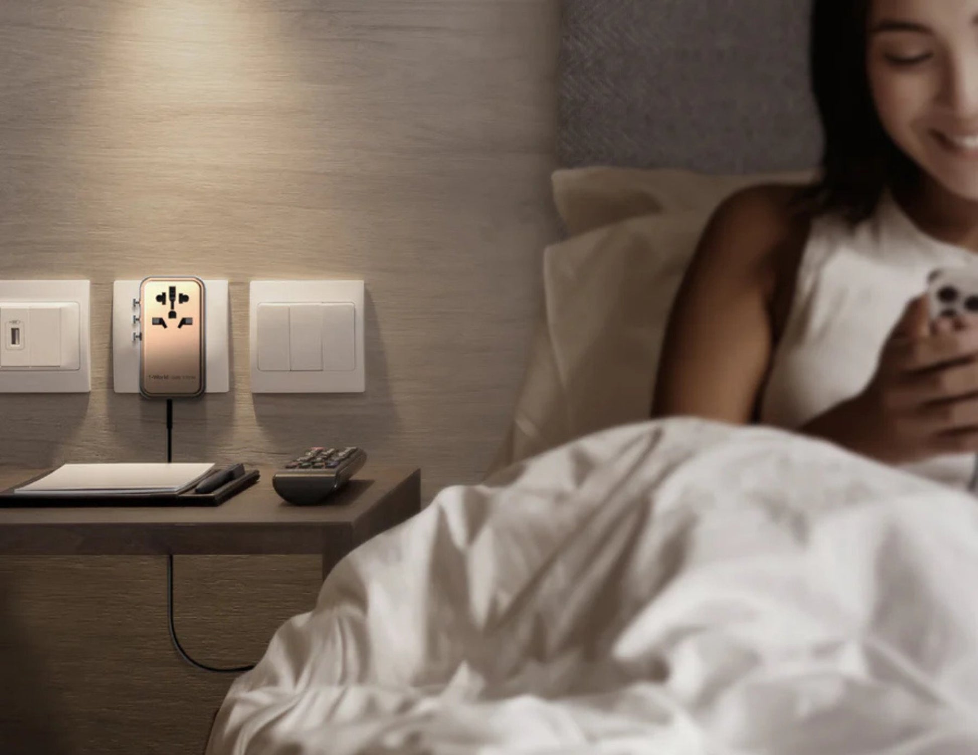 Woman in bed using a smartphone with a nightstand featuring electrical outlets and switches.