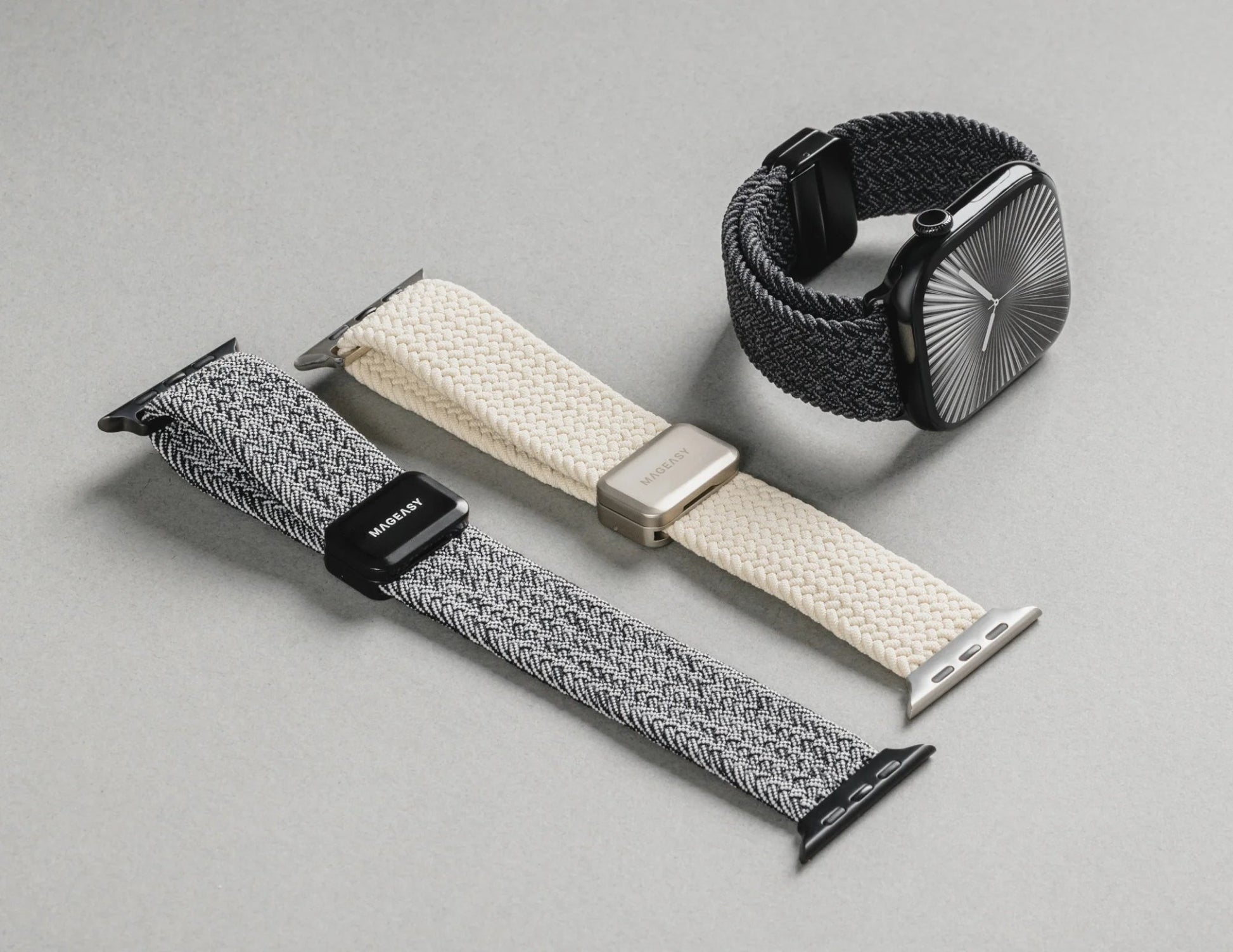 Three Apple Watch bands in different styles on a gray surface.