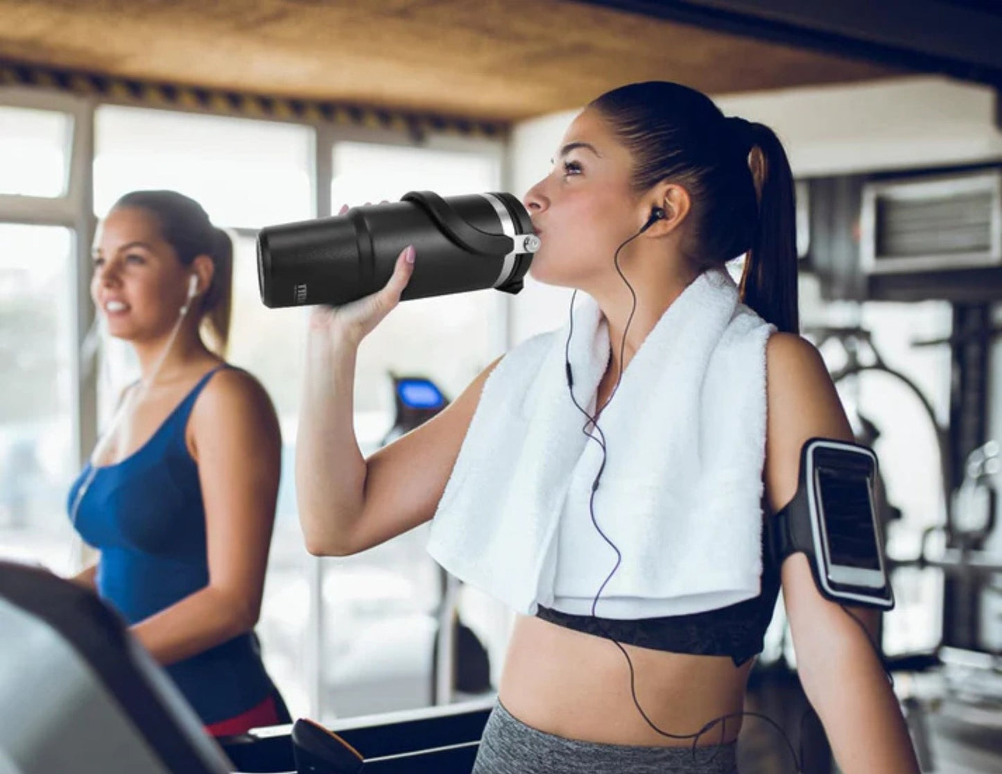 Woman in a gym drinking from a Tyeso TS-8828 Vacuum Insulated Tumbler 900ML with another person in the background.