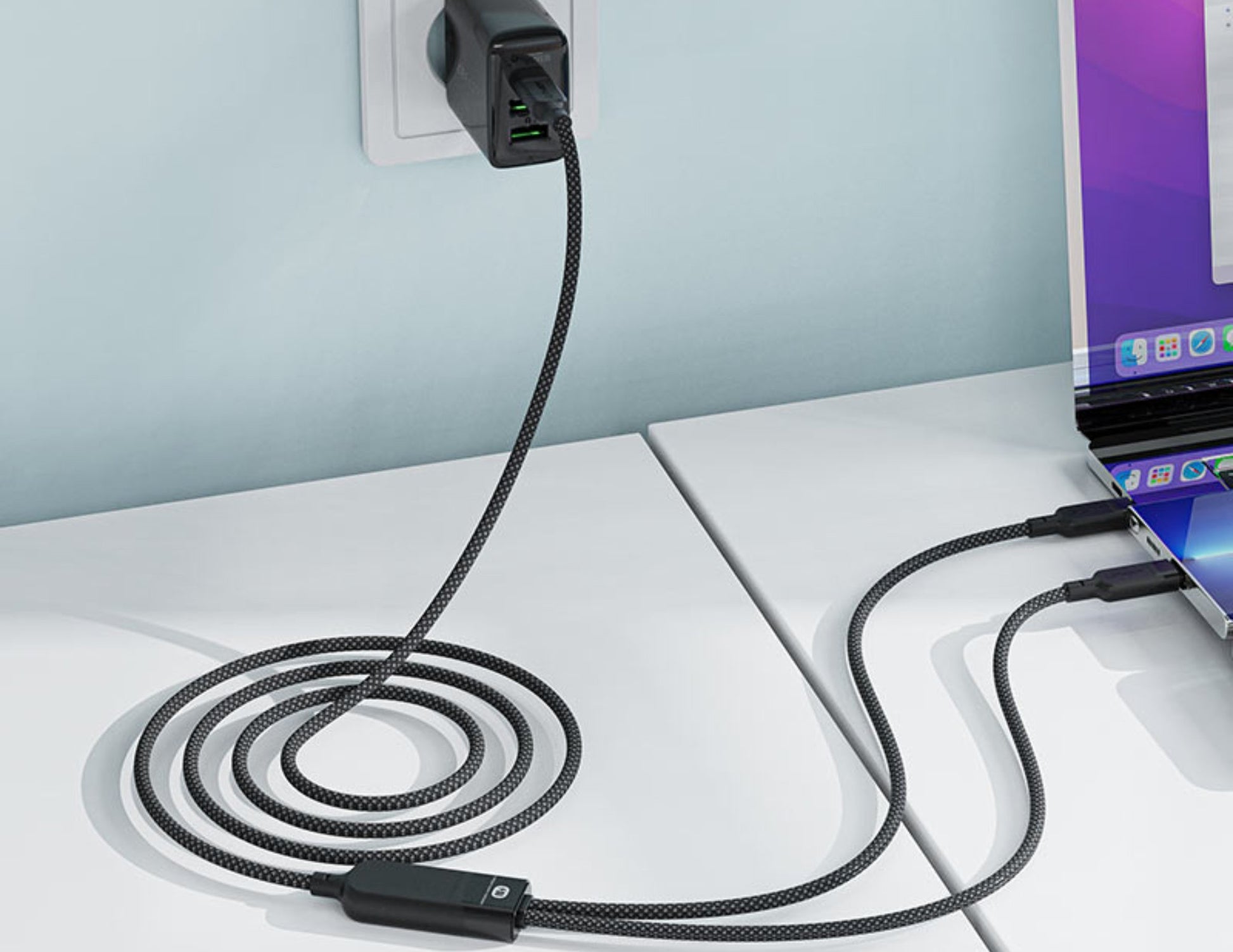 Black braided cable plugged into a laptop and wall outlet on a white surface.