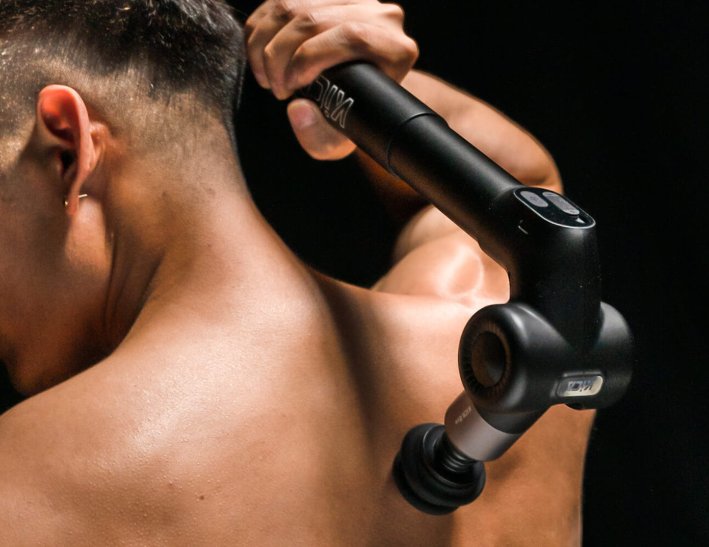 Person using a Kica Evo Fascia Massage Gun on their back against a dark background