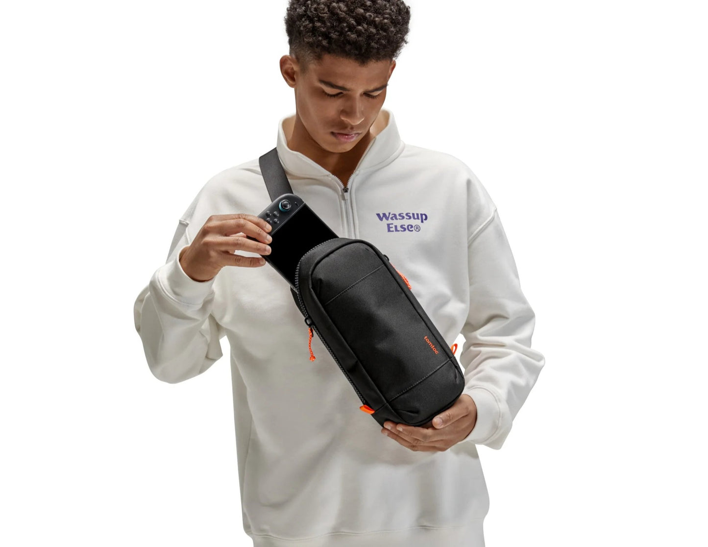 Person wearing a white hoodie with text holding a Tomtoc GameOn-G49 Nintendo Switch 2 Sling Bag – Black (G49S1D1) on a white background