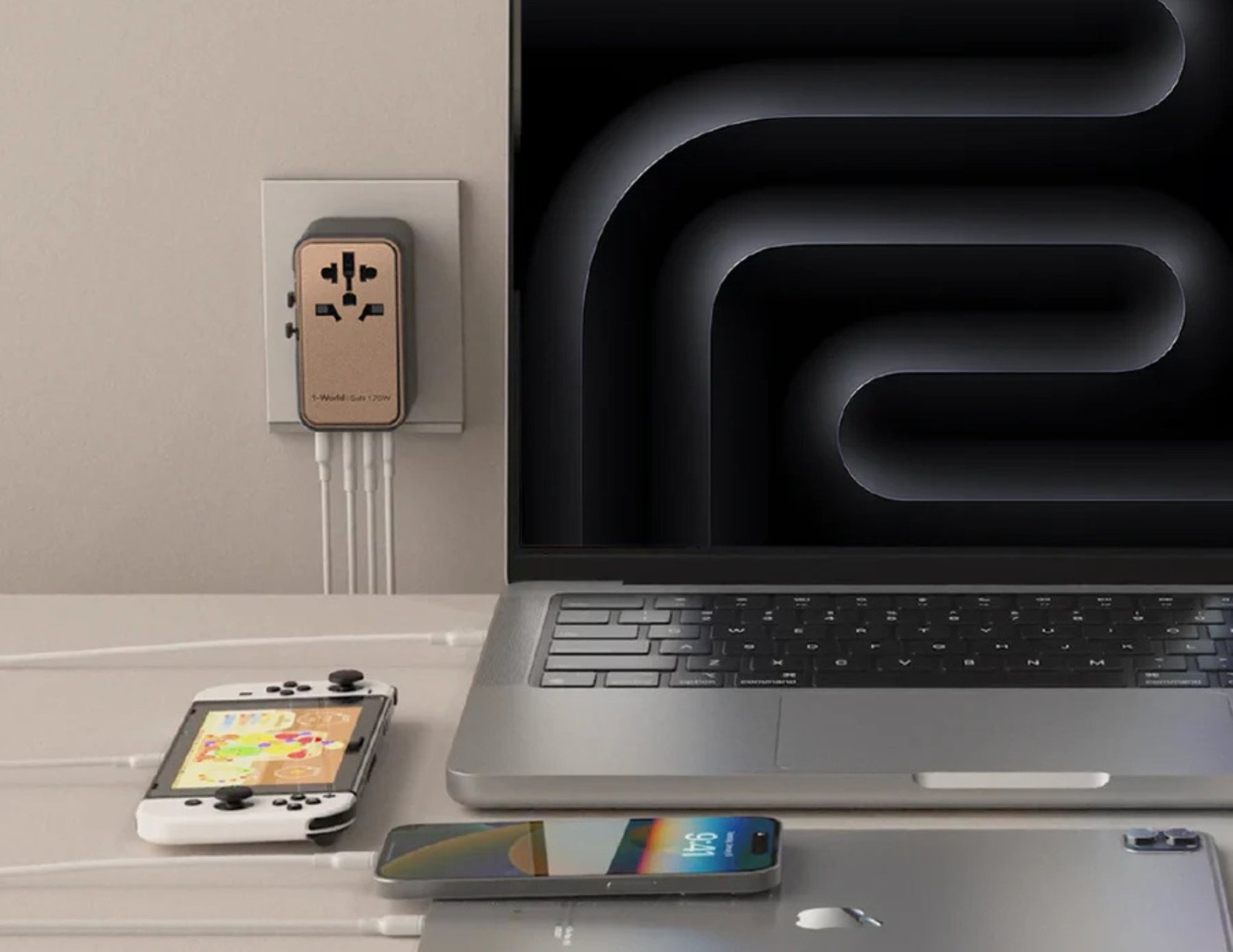 Laptop, smartphone, and gaming console on a desk with a power adapter in the background.