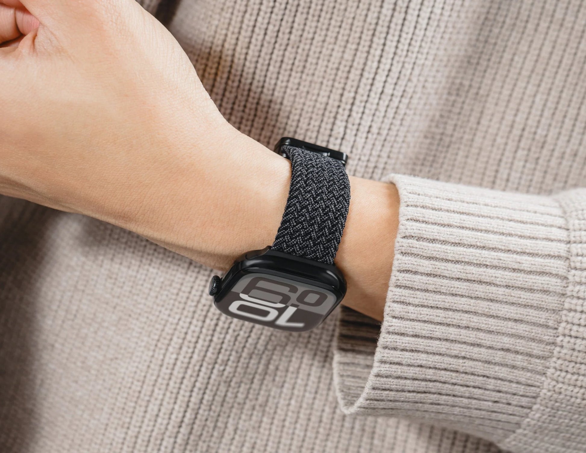 Smartwatch with black band on person's wrist wearing beige sweater