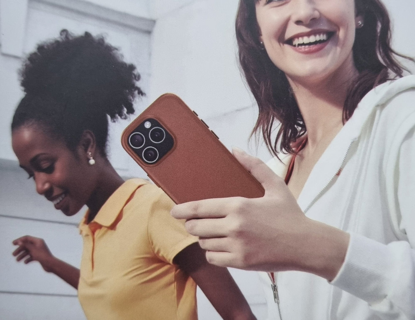Two women looking at a phone with a brown case outdoors.
