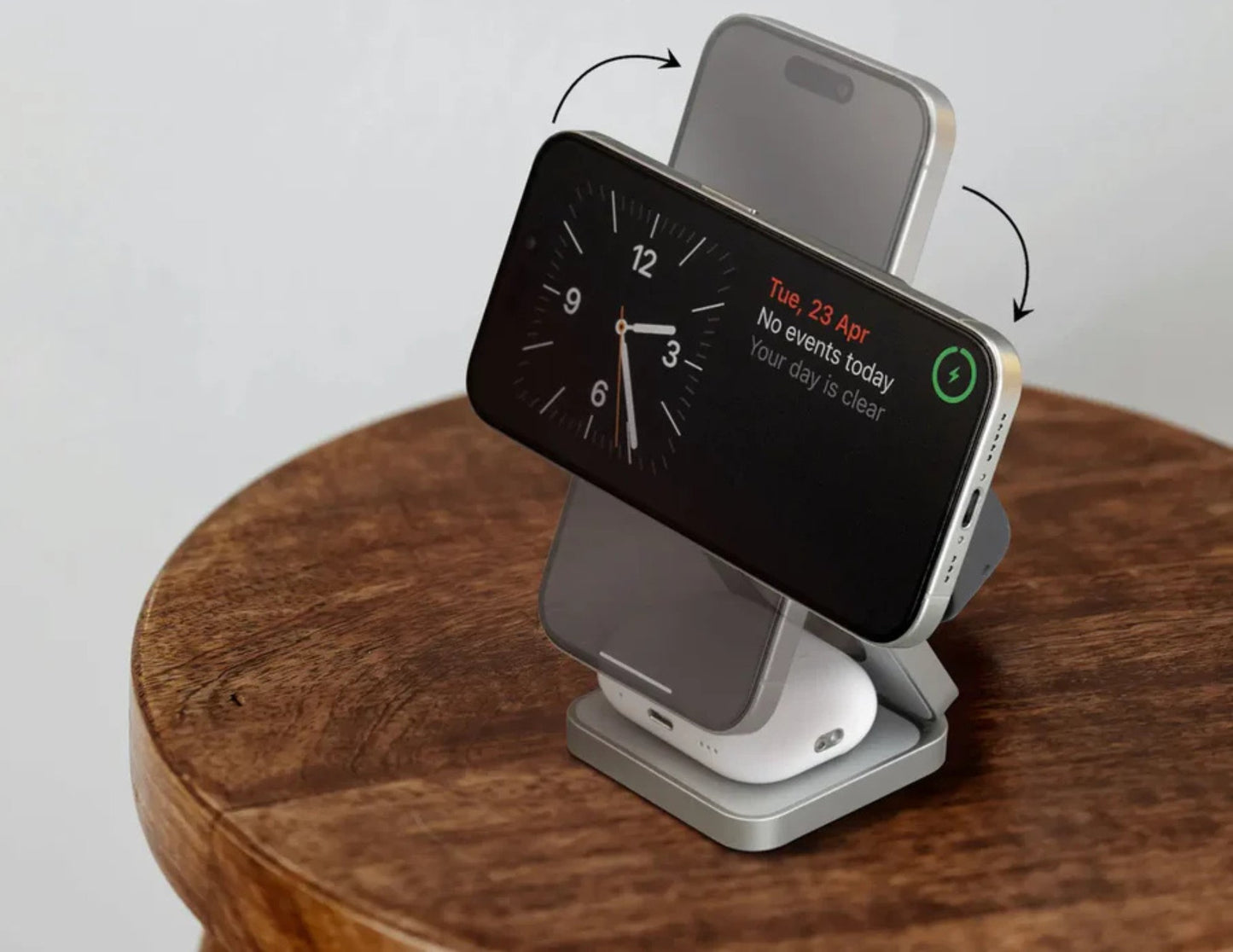 Multi-device charging stand with smartphone, smartwatch, and wireless charger on a wooden surface.
