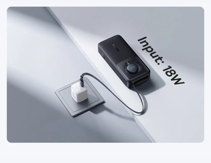 Black electronic device with a cable plugged into a white square socket on a light gray background.