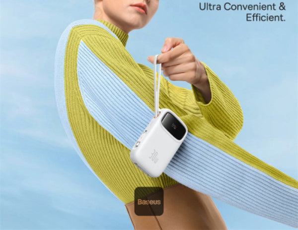 Person wearing a yellow sweater holding a white device with 'Baseus' branding against a blue sky.