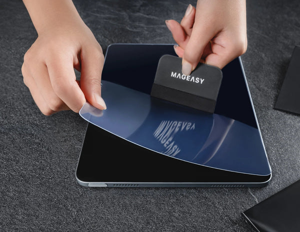 Person applying a screen protector to a device on a dark surface.