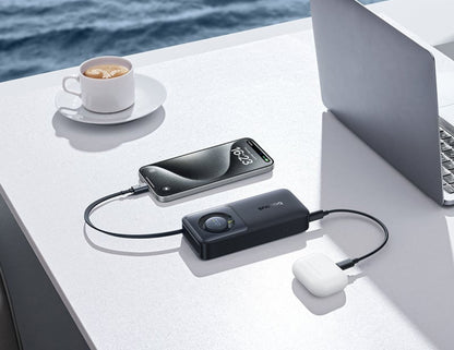 Laptop, smartphone, and power bank on a table with a cup of coffee and scenic background.