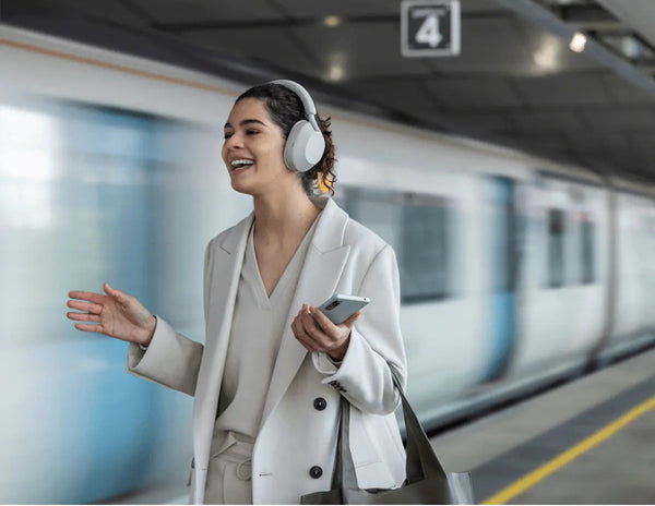 Woman wearing headphones and holding a phone at a train station