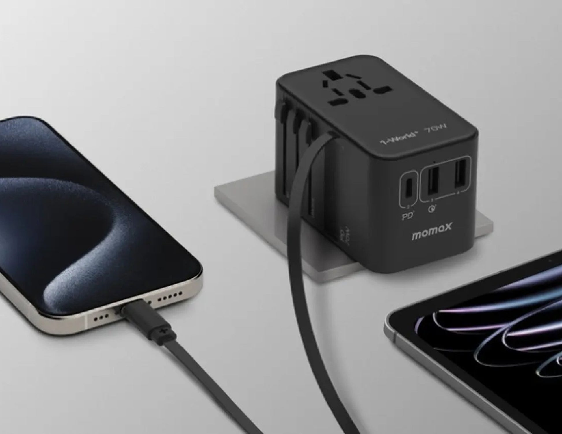 Black Momax 1‑World+ 70W GaN 3‑Port Travel Adapter with Retractable USB‑C Cable – UA18 connected to a smartphone and tablet on a light gray background.