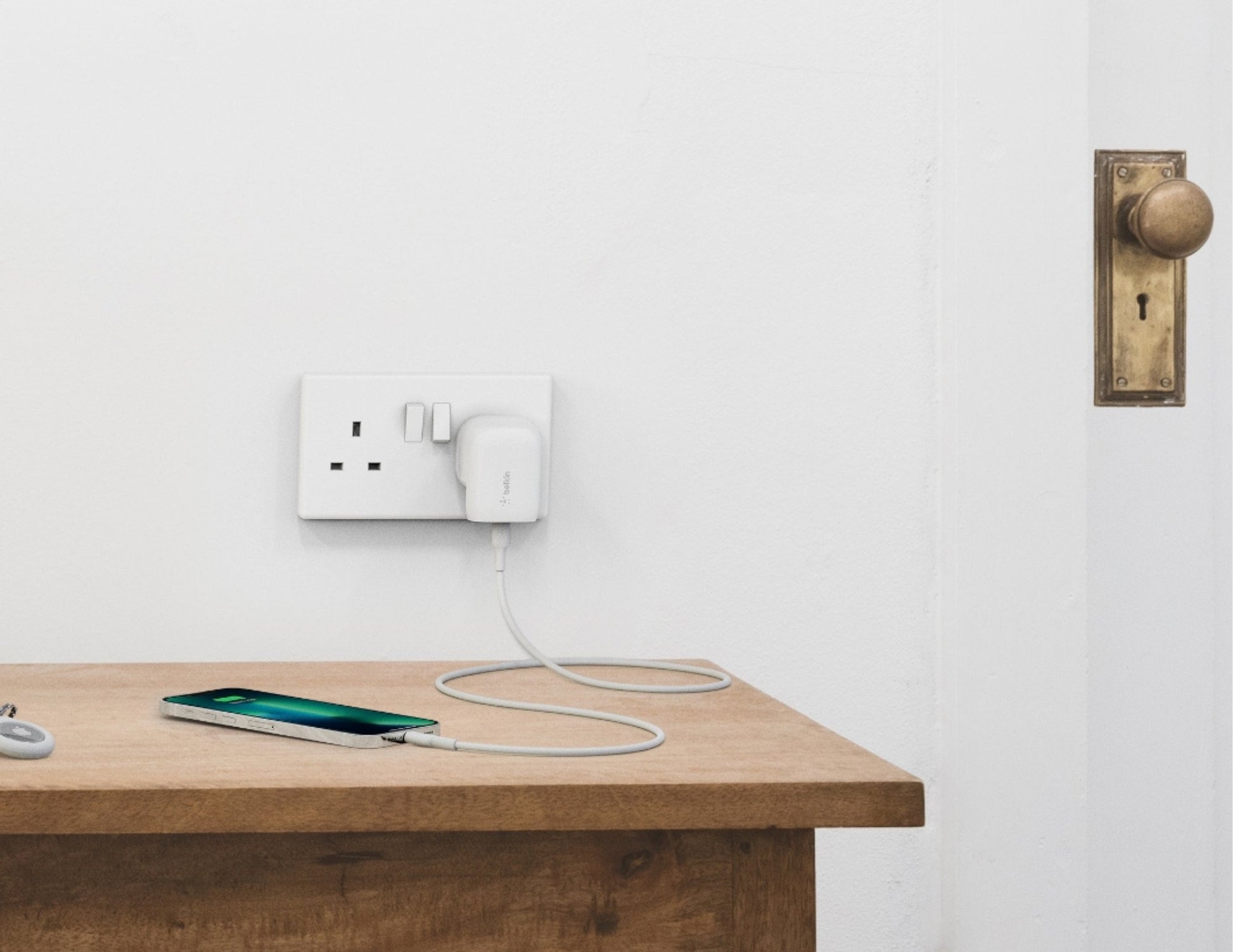 Phone charging on a wooden table with a white wall and brass door handle in the background