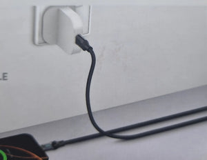 Black cable plugged into a white wall socket on a light gray surface.
