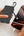 Person using a black portable charger to power a smartphone on a light gray background