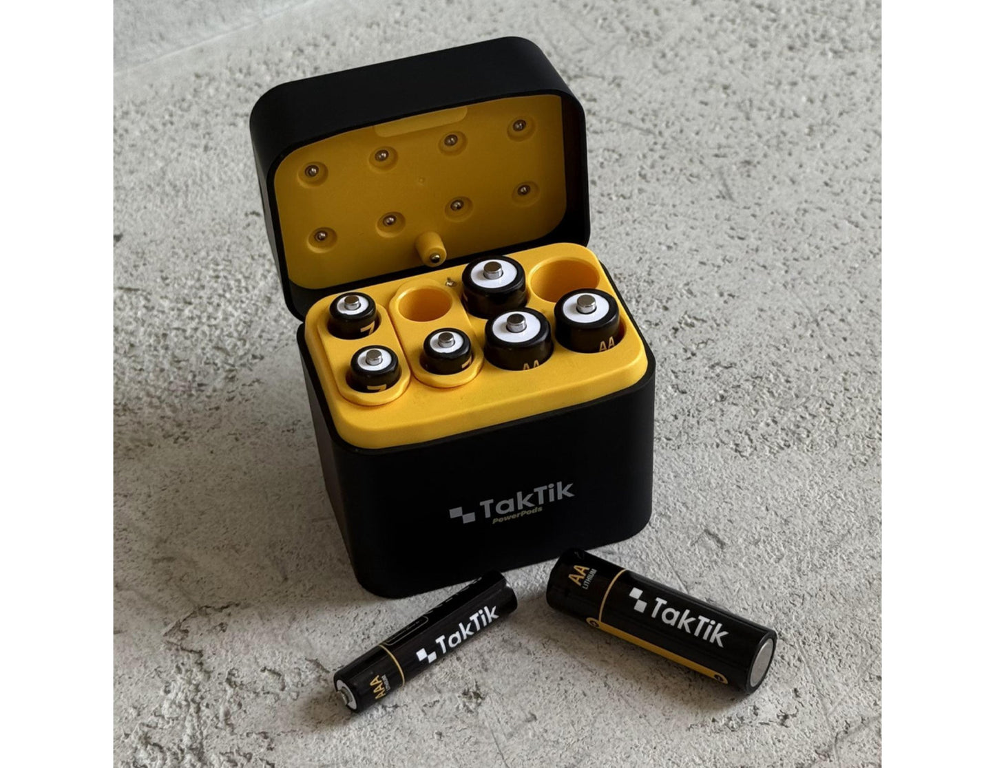 Black and yellow TakTik battery case with batteries on a concrete surface