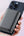 Hand holding a smartphone with a black case against a light pink background