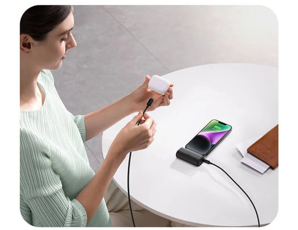 Woman using a smartphone with a Baseus Compact Fast Charging Power Bank iP Edition on a table.
