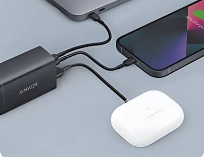 Anker power bank charging a smartphone, tablet, and wireless earbuds on a gray surface.