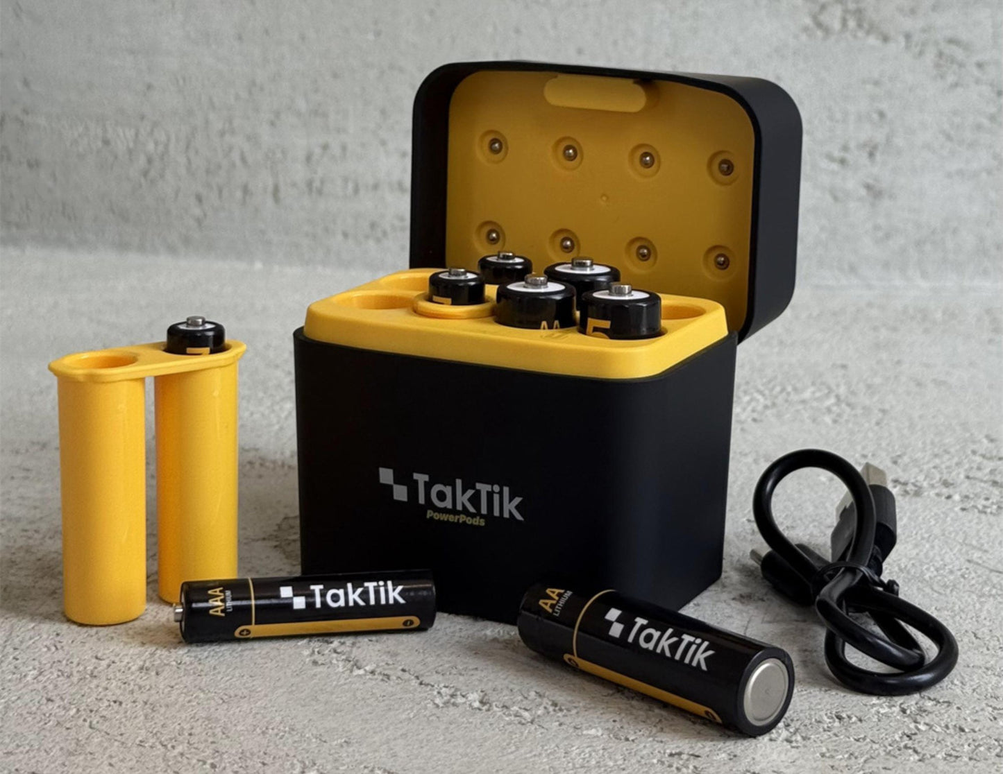 TakTik battery pack with batteries and charger on a gray surface