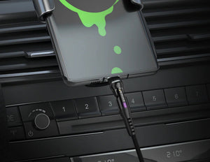 Phone case with green accents attached to a car vent, charging cable visible.