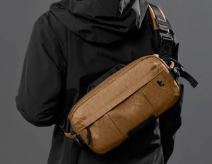 Person wearing a black jacket with a Tomtoc Wander-T26 X-Pac Daily Sling Bag – Brown (T26S1K1) on a gray background