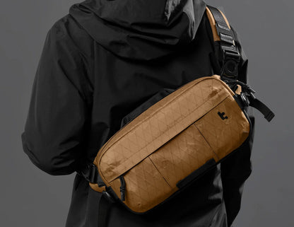 Person wearing a black jacket with a Tomtoc Wander-T26 X-Pac Daily Sling Bag – Brown (T26S1K1) on a gray background