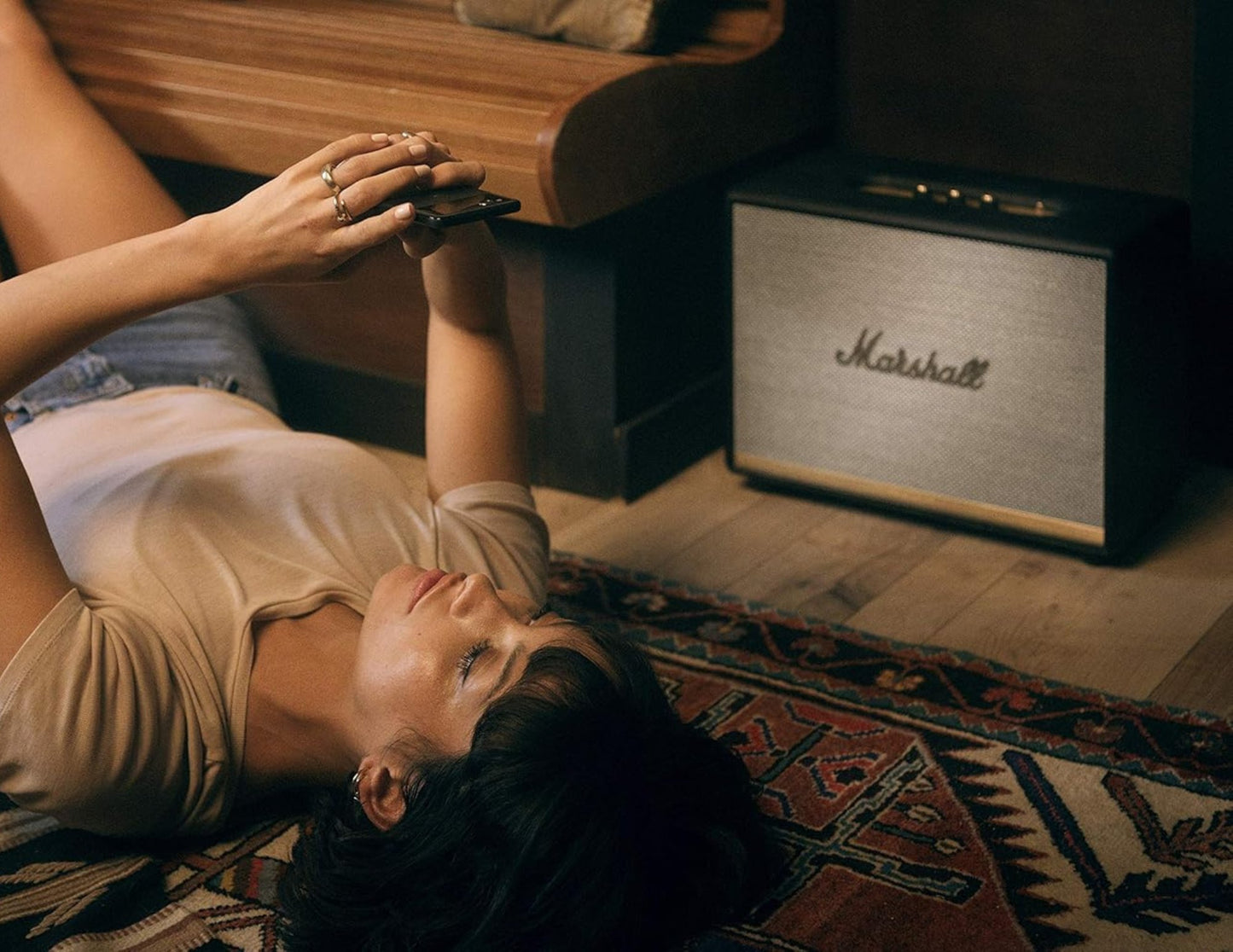 Person lying on a rug next to a Marshall speaker in a room.