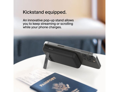 Belkin BoostCharge Magnetic Wireless Power Bank 5000mAh with Fold-out Stand – BPD004btBK – Black on a table next to a passport