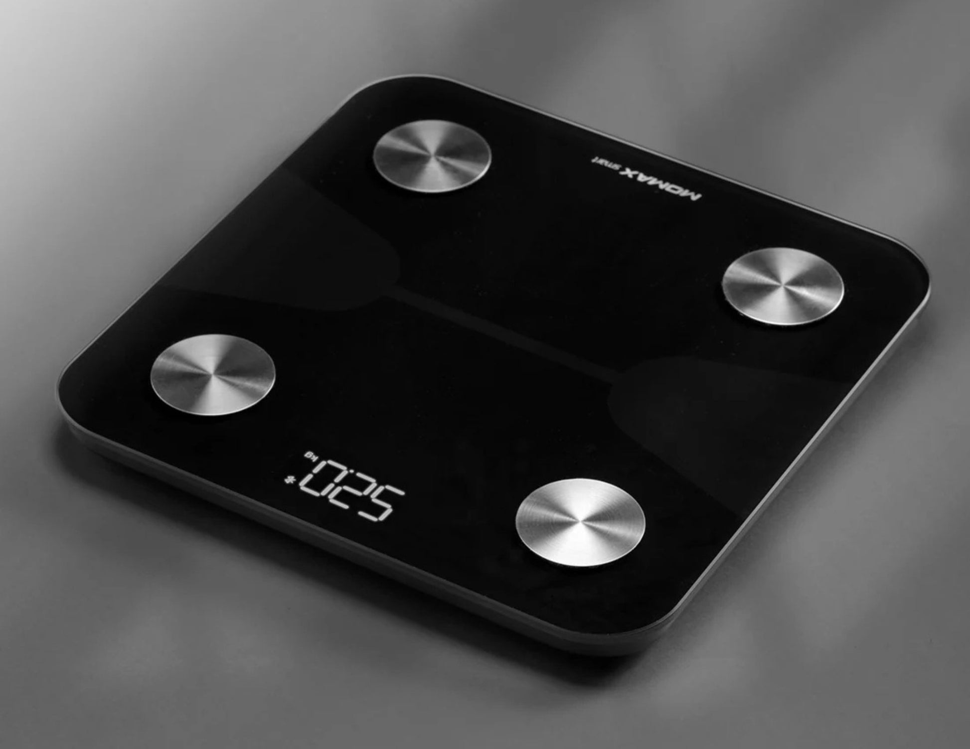 Black digital bathroom scale with silver buttons on a gray background