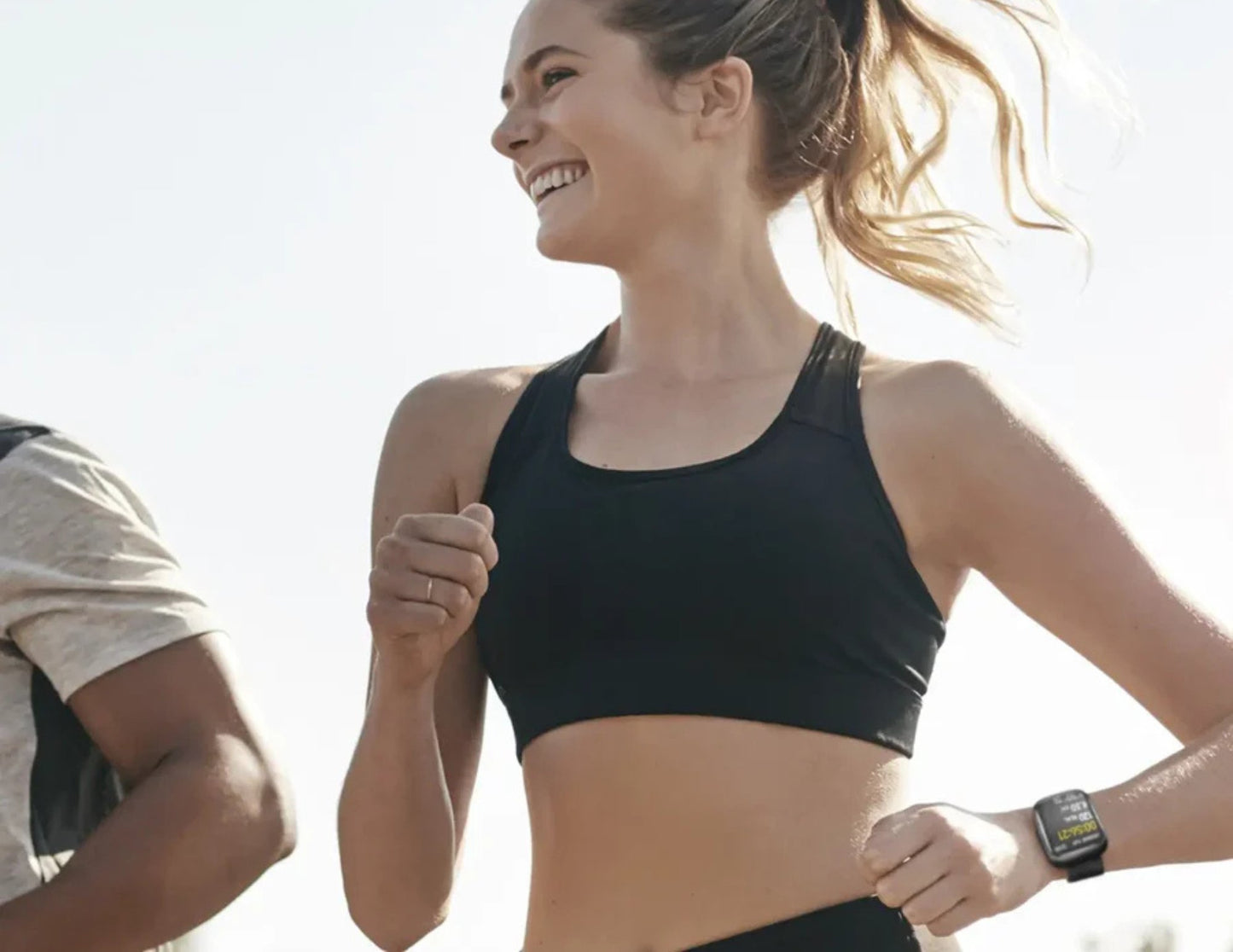 Woman in athletic wear running outdoors with a clear sky background