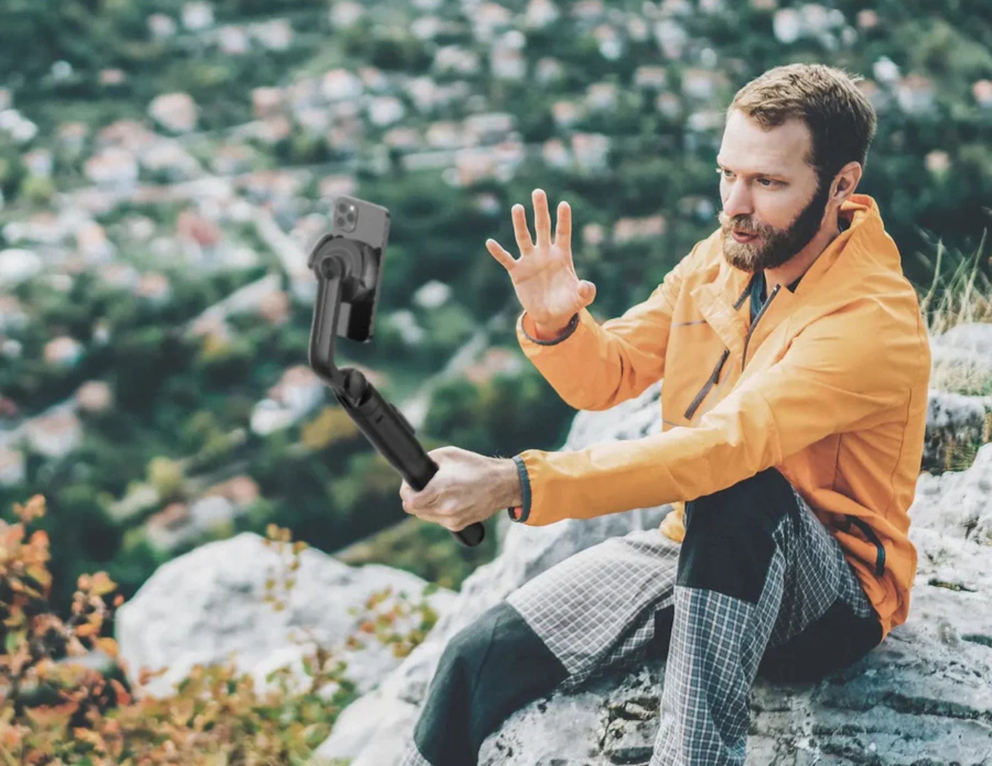 Man in an orange jacket using a Momax 1-Snap Pole Magnetic Tripod Selfie Stick with Wireless Remote – KM17D in a mountainous area