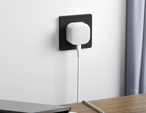 White smart plug on a black wall socket with a white cable, against a light gray wall.