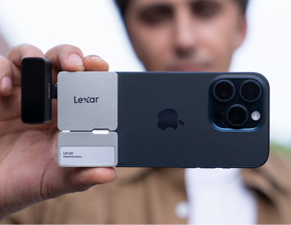 Person holding a smartphone with a Lexar card reader attached, blurred background
