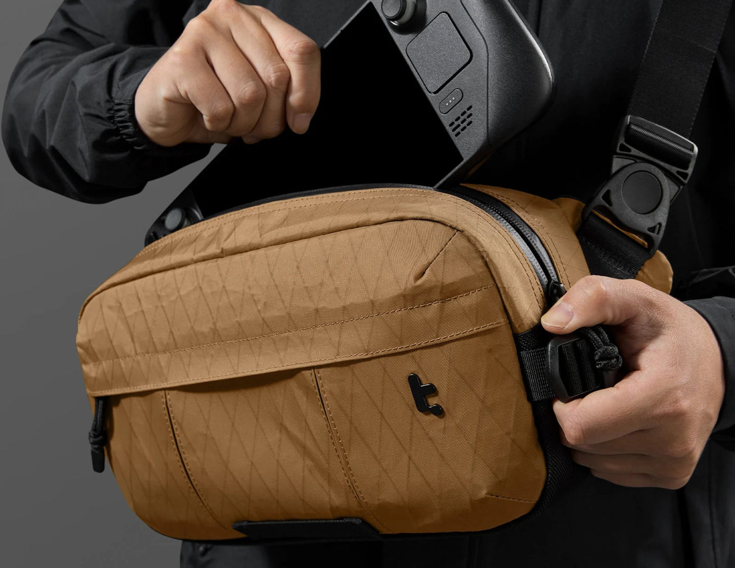 Person holding a Tomtoc Wander-T26 X-Pac Daily Sling Bag – Brown (T26S1K1) with a camera, against a dark background