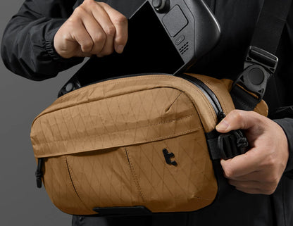 Person holding a Tomtoc Wander-T26 X-Pac Daily Sling Bag – Brown (T26S1K1) with a camera, against a dark background