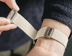 Person adjusting a beige fabric strap on a wrist.