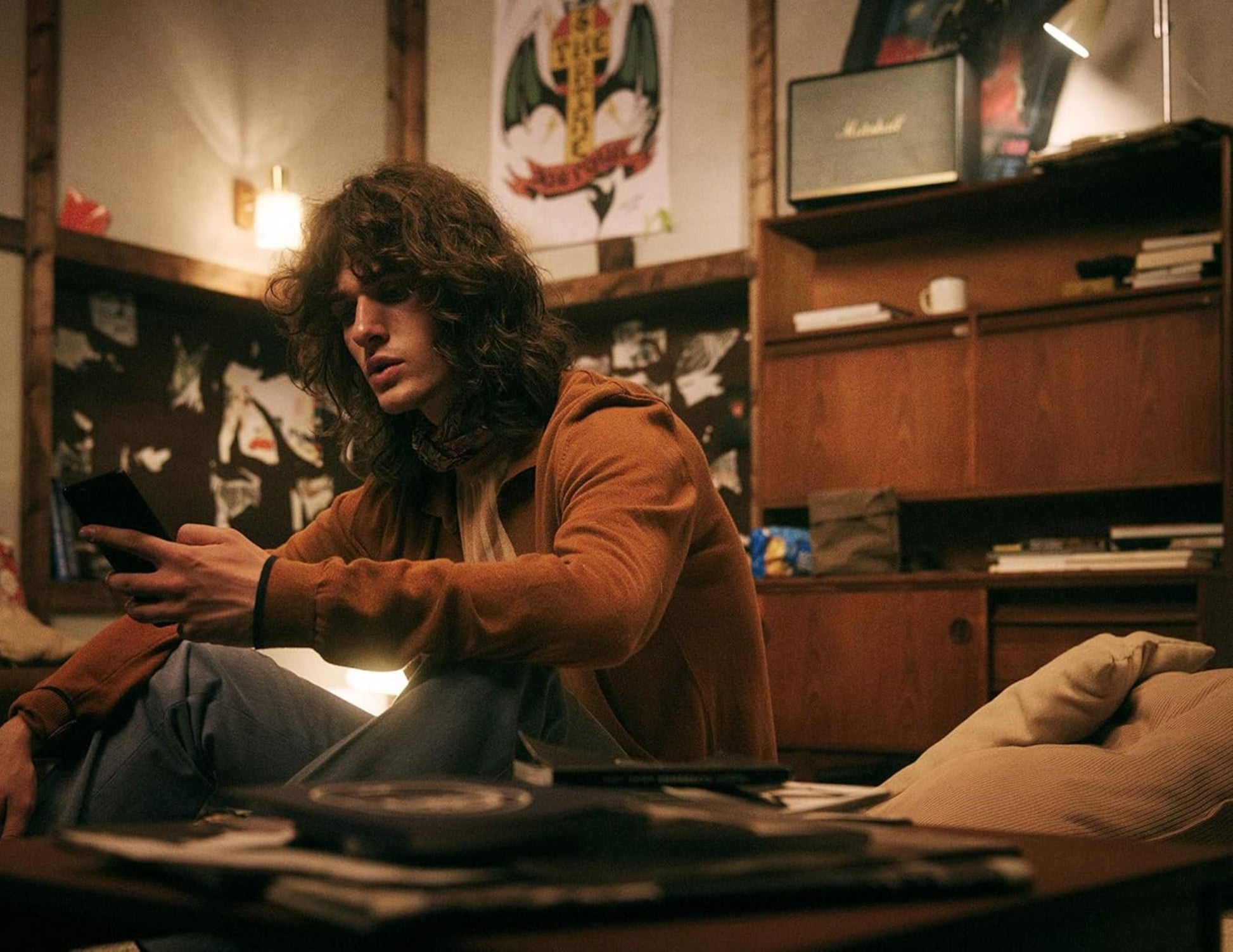 Person sitting in a room with posters and a record player, holding a phone.
